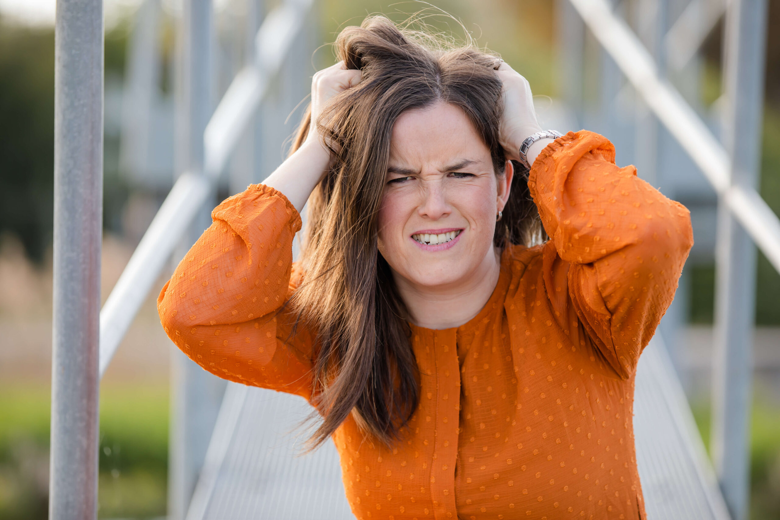 Porträt einer braunhaarigen Frau in orangenem Kleid, die sich verzweifelt die Haare rauft